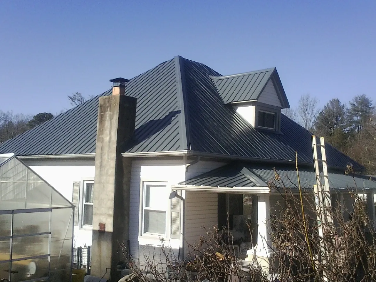 Dark blue standing seam metal roof on a white farmhouse with dormer — Slate & Tile Roof Repair by Roofing Brothers in Berwyn